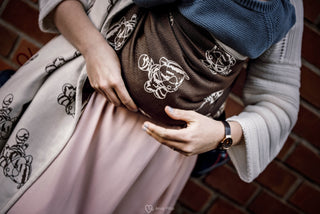 What is a Ring Sling and What Do I Need To Know Before Buying One? Image is a woman carrying a baby in a brown and creme ring sling with cartoon cat images. The ring sling is Lenny Lamb brand, print Marysia's Cat