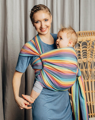 Model wearing a child inward facing in the front with a long woven wrap. Model is turned toward thee camera while the model looks at the camera just shy of holding the foot of the distracted child. The print is Luna