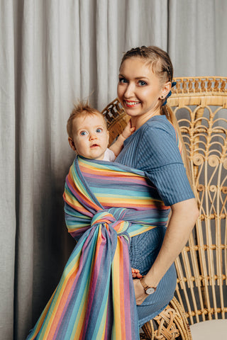 Model wearing a child inward facing in the front with a long woven wrap. Model is turned to their right side while both model and child look at the camera . The print is Luna