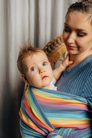 Model wearing a child inward facing in the front with a long woven wrap. Models head is partially visible with a focus on the child in the carriers face. The print is Luna
