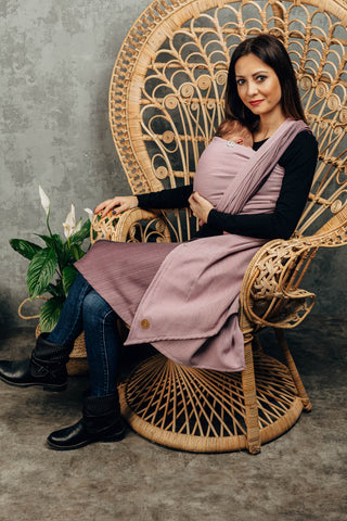 Model front wearing newborn (Inward facing) in long woven wrap. Print Little Herringbone Ombre Pink. Model is seated at a slight angle looking at the camera. 