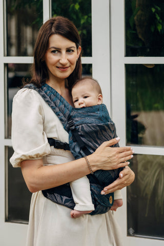 Woman holding her baby in a LennyLight Carrier. Featuring the Rainforest Nocturnal Design