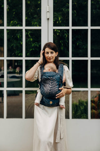 Woman holding her baby in a LennyLight Carrier. Featuring the Rainforest Nocturnal Design