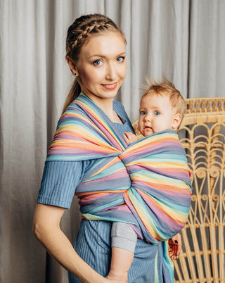 Model wearing a child inward facing in the front with a long woven wrap. Model is turned to their right side while both model looks at the camera . The print is Luna