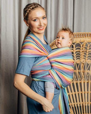Model wearing a child inward facing in the front with a long woven wrap. Model is turned to their right side while both model looks at the camera . The print is Luna