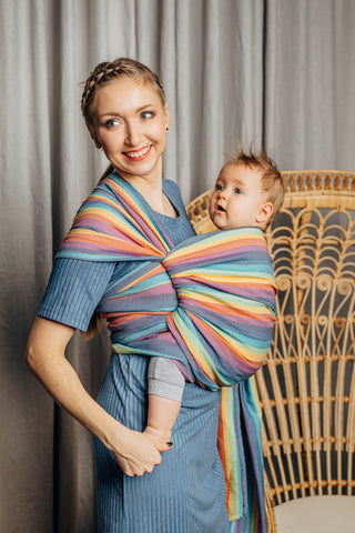 Model wearing a child inward facing in the front with a long woven wrap. Model is turned to their left side while both model and child look to the left of the picture . The print is Luna