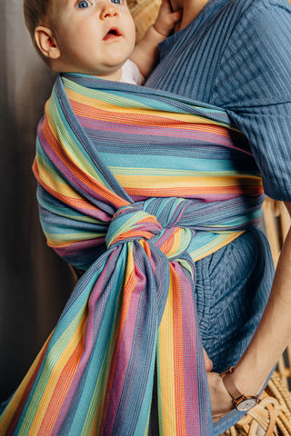 Model wearing a child inward facing in the front with a long woven wrap. Childs head is partially visible with a focus on the knot of the carry. The print is Luna