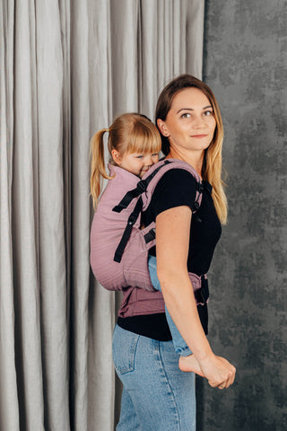 Preschool carrier in Little herringbone - Ombre Pink. Model and child side profile looking  at camera. Child is being back carried. 