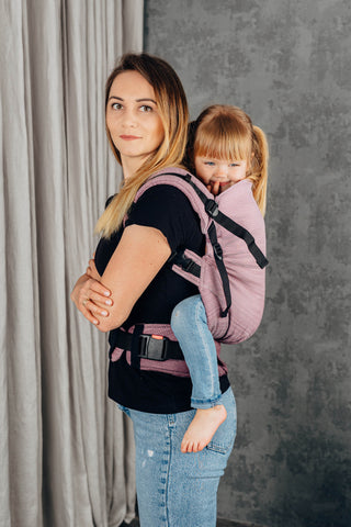 Preschool carrier in Little herringbone - Ombre Pink.Model and child side profile looking  at camera. Child is being back carried. 