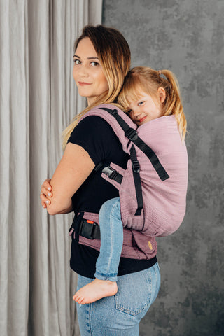 Preschool carrier in Little herringbone - Ombre Pink.Model and child side profile looking  at camera. Child is being back carried. 