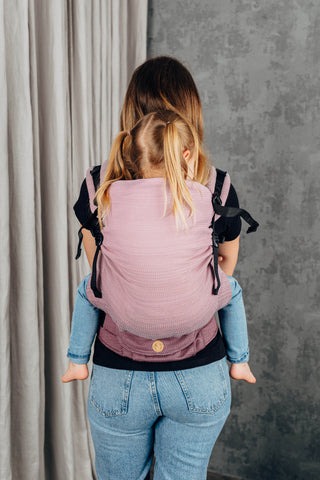 Preschool carrier in Little herringbone - Ombre Pink. Model and child behind profile looking away camera. Child is being back carried. 