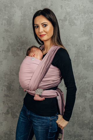 Model front wearing newborn (Inward facing) in long woven wrap. Print Little Herringbone Ombre Pink. Model is standing at a slight angle looking at the camera. 