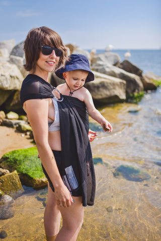 Model wears toddler in black water ring sling lakeside