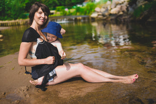 Model wears toddler in black water ring sling lakeside