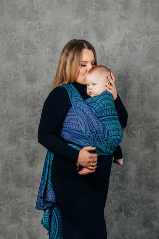 Mother kisses child in Front Wrap Cross Carry in long woven wrap print Peacock's Tail Provance
